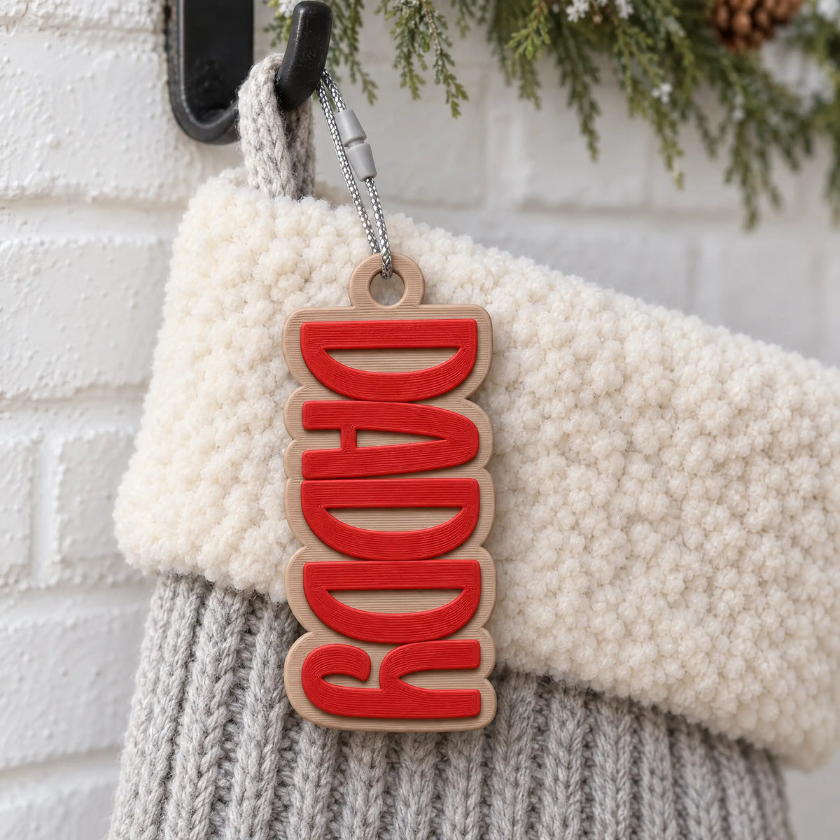 Block Letter Christmas Stocking Name Tag: red block capitals on a tan backing, name DADDY, on a knit Christmas stocking