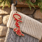 Modern Script Christmas Stocking Name Tag: red script on a white backing, name Cheryl, on a knit Christmas stocking